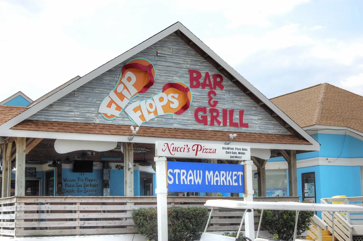 A lively exterior scene featuring the Flip Flops Bar & Grill sign along with Straw Market and Nucci's Pizza signs. The area suggests an inviting hub for dining, socializing, and live music, bustling with opportunities for group get-togethers.