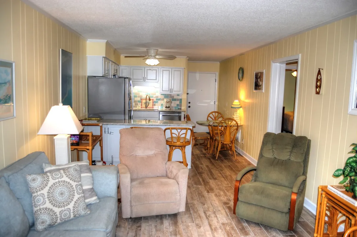 An inviting open-plan space featuring a sofa and recliner, a dining table, and a glimpse of the adjoining kitchen. The arrangement is ideal for socializing, dining, and relaxing, with enough space for everyone to gather comfortably.