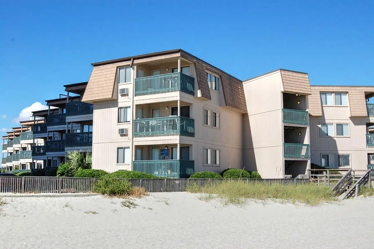 A scenic exterior view of a beachfront property showcasing private balconies overlooking lush landscaping and inviting sandy shores. The image captures the tranquil atmosphere ideal for peaceful beach walks, relaxation on balconies, and family gatherings by the sea, with the morning sunrise adding warmth to the scene.